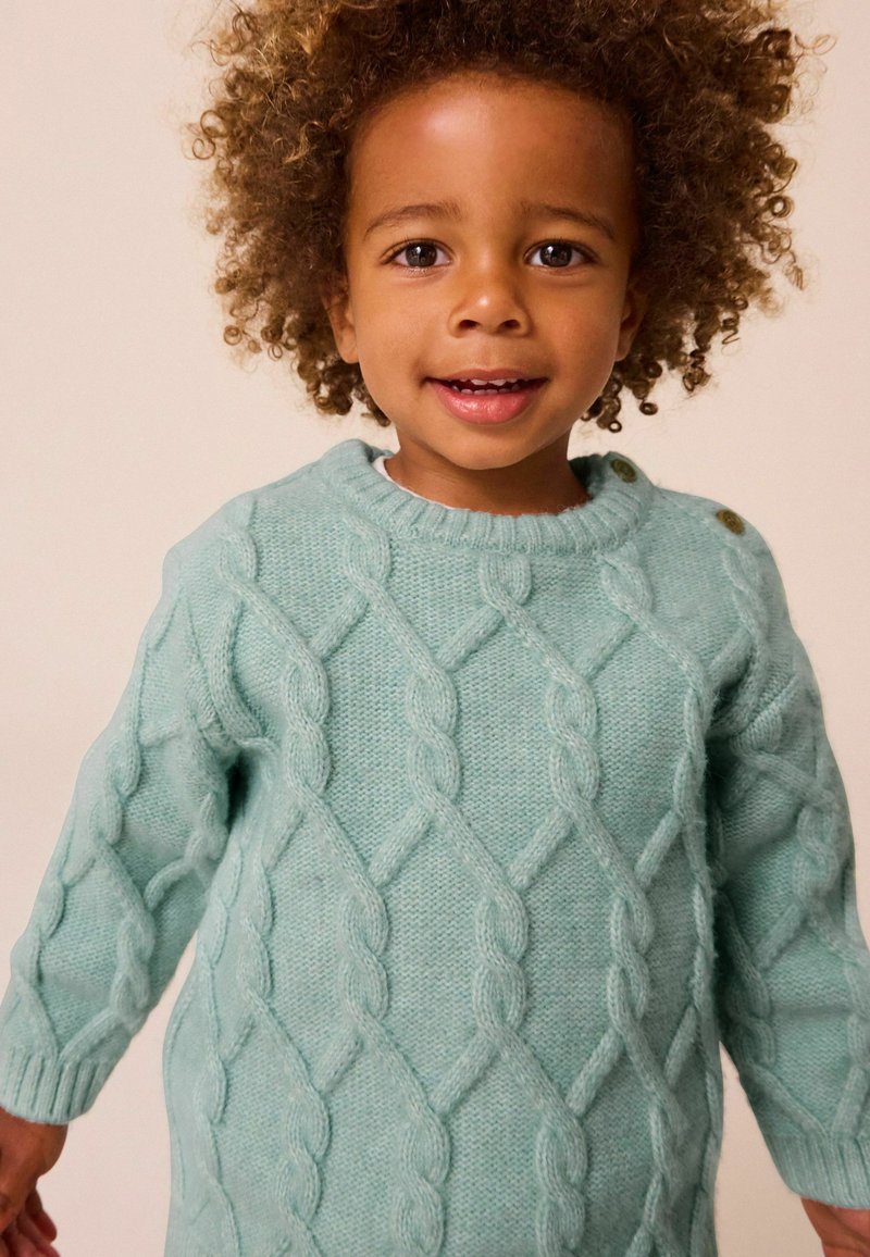 Pull en tricot bleu clair avec un motif en relief, col rond et couture visible. Comprend deux accents de bouton sur l'épaule.