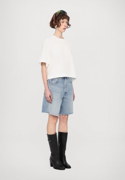 Valge lühikeste varrukatega t-särk, helesinised denim lühikesed püksid rebenenud äärega ja mustad põlvikud kõrged kontsad. Värviline triibuline peapael juustes.