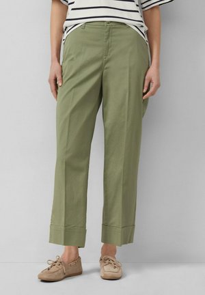 Osoba w oliwkowozielonych szerokich, skróconych spodniach z dużymi mankietami, w paskowanej koszuli i beżowych mokasynach na sznurowadła.