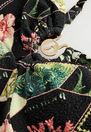 Tissu noir à motif floral, texturé avec des bords froncés, comportant un accent en métal doré et un cordon élastique.