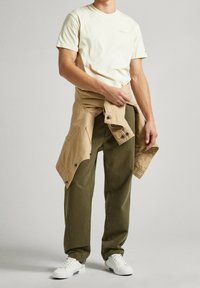 Beige puuvillane t-särk, rohelised puuvillased püksid ja beež jakk, mis on taljel seotud. Valged tossud tumedate tallatoodetega.