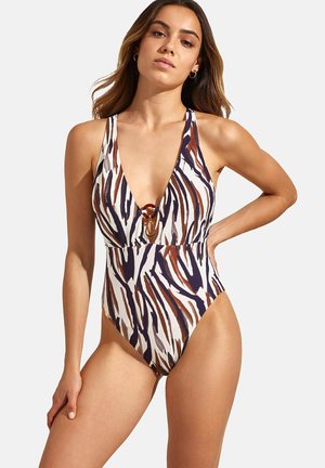 Maillot de bain une pièce avec un décolleté en V profond, imprimé zèbre marron et bleu marine, détail découpé avec un accessoire circulaire et une silhouette ajustée.