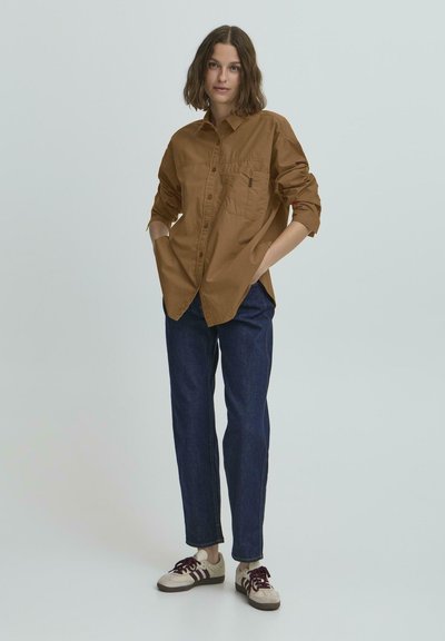 Bruine overhem Collarshirt met een voorzak, gecombineerd met donkerblauwe tapered jeans en grijze sneakers met bordeauxrode accenten.