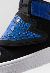 Černá teniska s modrým koženým akcentem a logem křídla. Bílá gumová podrážka a textilní svršek dotvářejí design.