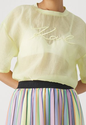 Doorzichtige lichtgele top met korte mouwen en "Love" borduurwerk, gecombineerd met een geplooide rok met hoge taille en verticale pastelstrepen.