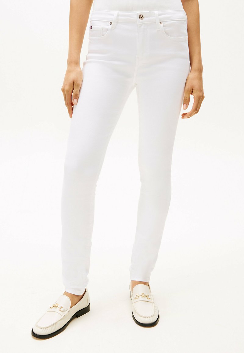 Hvite trange jeans laget av denim, med knappestolpe, fem-lomme-design og subtil søm. Kombinert med hvite loafers.