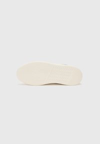 Hvite sneakersåler med et teksturert grep-mønster, har en glatt overflate og en avrundet tådesign.