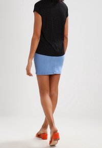 Černý vzorovaný top s krátkým rukávem spárovaný s modrou džínsovou mini sukní. Oranžové sandály na podpatku. Zaměřeno na pohled zezadu, ukazuje detaily outfitu.