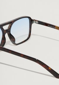 Gafas de sol de carey con lentes de tono azul, con un marco grueso y un logotipo de PIER.ONE en el lateral. Acabado suave y diseño angular.