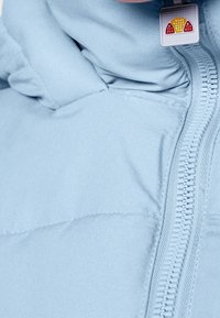 Jasnoniebieska kurtka puchowa z wysokim kołnierzem, pełnym zamkiem błyskawicznym i małą metką z logo w pobliżu zamka. Gładka tekstura tkaniny, bez wzorów.