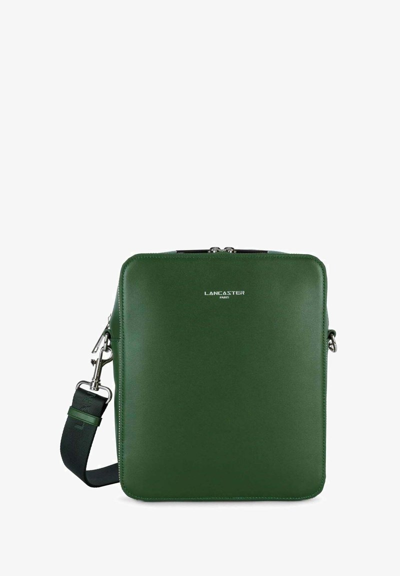 Sac carré en cuir vert avec une texture lisse, featuring des ferrures en argent et une bandoulière amovible. Nom de la marque "LANCASTER PARIS" embossé sur le devant.