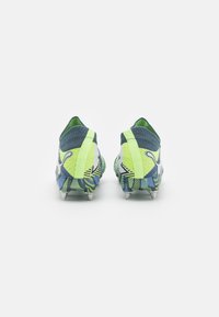 Scarpe da calcio con una parte superiore testurizzata blu e verde, accenti giallo brillante e una suola a motivi con tacchetti argentati.