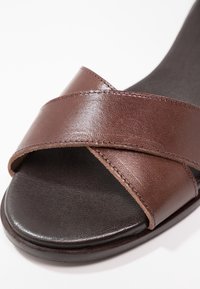 Sandale en cuir marron avec deux brides croisées sur une semelle intérieure noire texturée et un design à bout ouvert arrondi.