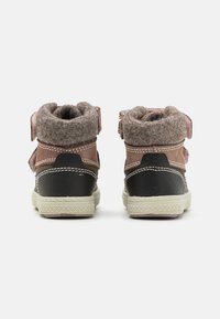 Bottines marron foncé et beige avec un col en feutre gris doux, des sangles ajustables et un talon noir texturé. Semelles en caoutchouc et coutures blanches.