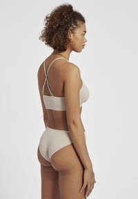 Beige ribbad bh och matchande trosor med justerbara korsade remmar och en sömlös design, visad från baksidan. Mjuk tygkänsla.