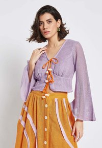 Lavender knitted cropped top with bell sleeves and orange drawstrings, paired with an orange button-down skirt featuring pink stripes.