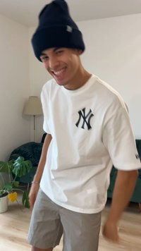 Wit T-shirt met korte mouwen met een zwart New York Yankees-logo, gecombineerd met lichtgrijze shorts en een zwarte gebreide beanie.