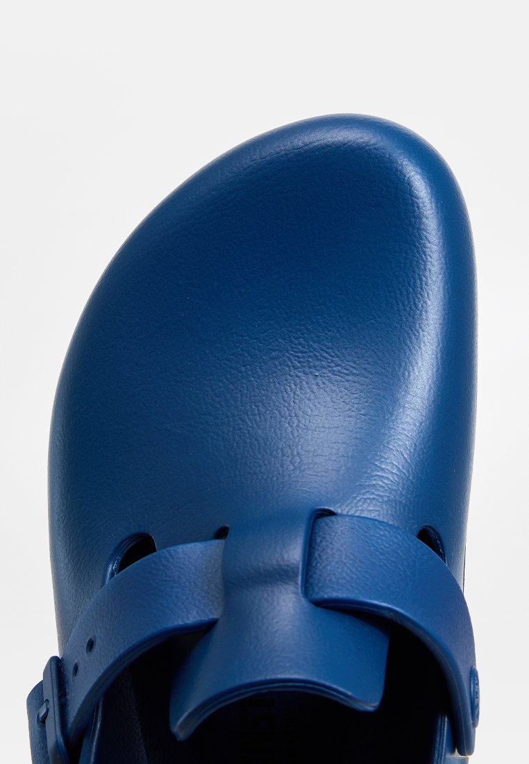 Obenansicht eines blauen, geschlossenen Clogs mit verstellbarem Riemen und matter Oberfläche auf einem weißen Hintergrund.