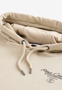 Sudadera beige con una capucha grande, dos cordones con puntas plateadas y texto bordado "Pima County Tucson Arizona" en la parte delantera.