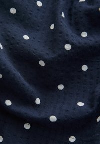 Marineblauer Stoff mit weißen Punkten, der eine strukturierte Oberfläche mit dezenten erhabenen Mustern aufweist. Das Material wirkt leicht und weich.