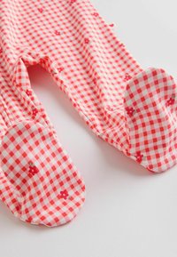 Leggings pour bébé à motifs vichy rouge et blanc, ornés de petites fleurs rouges, avec pieds intégrés, posés à plat sur une surface blanche.