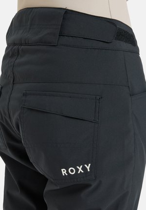 Crne snježne hlače od teksturiranog materijala, s leđnim džepovima s preklopima i čičak pojasom. Izvezeni "ROXY" logo u bijeloj boji.