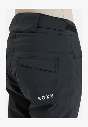 Schwarze Schnee-Hosen mit strukturiertem Stoff, Gesäßtaschen mit Klappen und einem Klettverschluss am Bund. Gesticktes "ROXY"-Logo in Weiß.