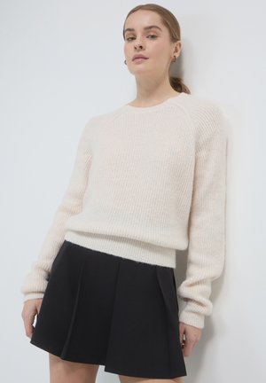 Maglione di colore crema a maglia con texture a coste e maniche lunghe, abbinato a una gonna plissettata nera. Entrambi i capi sono casual e aderenti.