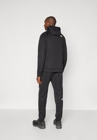 Černá sportovní mikina s kapucí na stažení, spárovaná s odpovídajícími slim-fit kalhotami. Obsahuje akcenty loga a odolnou tkaninu.