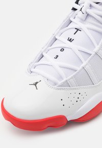 Chaussure de basket blanche et rouge avec logo Jumpman noir, dessus en tissu mesh, et texte "T W O 3" sur la languette sous les lacets.