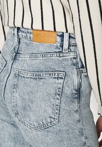 Ljusblå hög midja jeans i denim, med en läderlapp märkt "MONKI" på baksidan, med minimala sömnadsdetaljer.