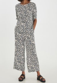 Completo due pezzi a fantasia in tessuto leggero. Presenta maniche corte, pantaloni a gamba ampia e una combinazione di macchie leopardate nere, bianche e beige.