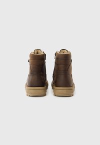 Brūni ādas potīšu zābaki ar mīkstu oderi, teksturētu virsmu, aizmugures rāvējslēdzējiem un gaiši brūnu gumijas zoli.