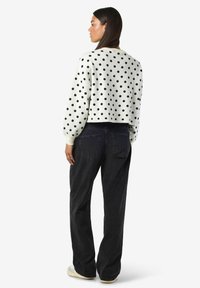 Balts cropped džemperis ar melnām punktiņām, ar garām piedurknēm un apaļu kakla izgriezumu, apvienots ar augsto jostasvietu melniem džinsiem.