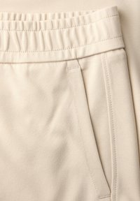 Pantalon de survêtement beige avec ceinture élastique, poche latérale et coutures visibles sur un tissu doux.