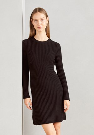 Black ribbed knit dress with long sleeves, round neckline, and a fitted silhouette, featuring vertical seams and a textured finish.
