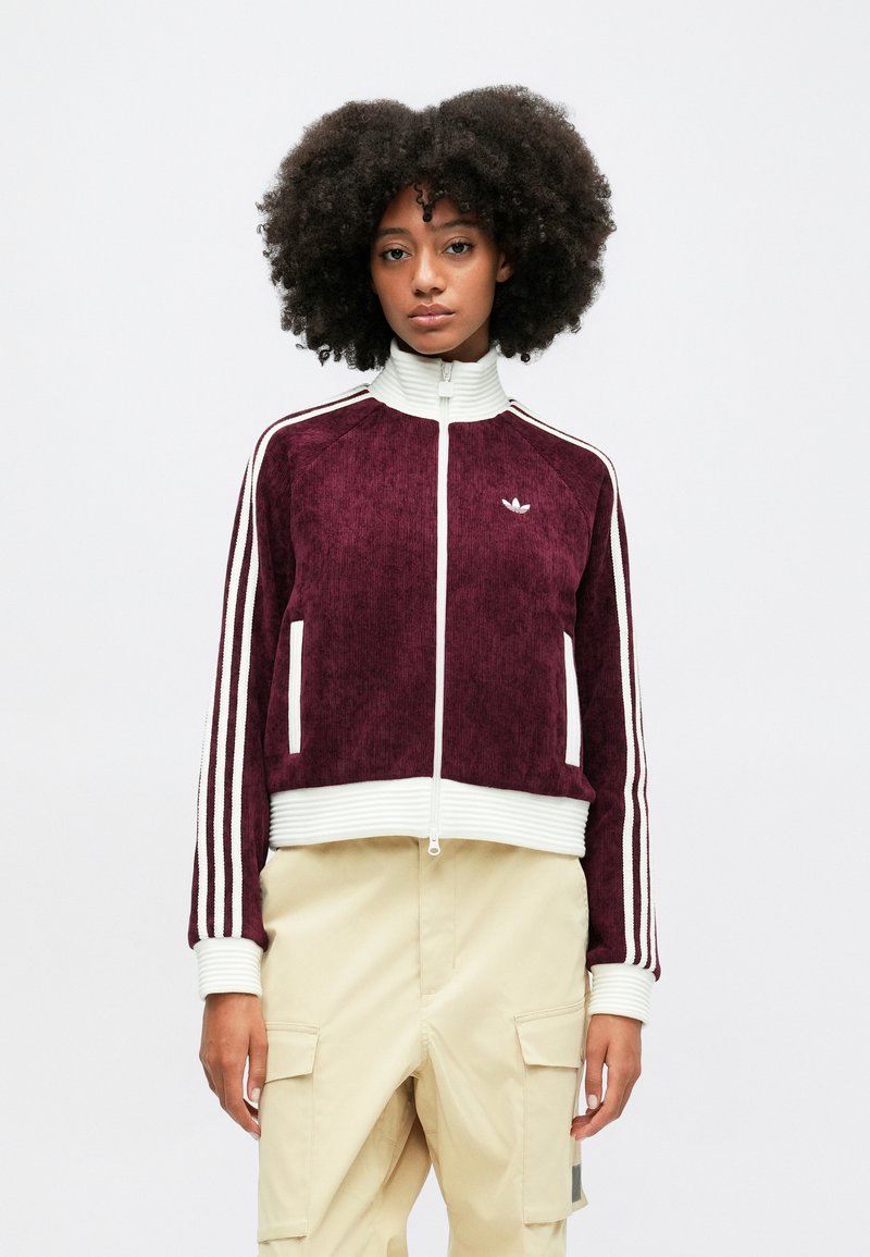 Burgundy zip-up jack met witte stripes, geribbelde kraag en manchetten, met een zachte textuur en twee zijzakken. Klein logo op de borst.
