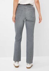Jean en denim gris avec une coupe droite, présentant des poches arrière et une texture lisse. Porté avec des chaussures blanches avec une semelle beige.