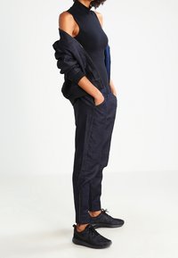 Czarny dopasowany kombinezon, lekka granatowa kurtka i ciemnoniebieskie dresy z zamkami na kostkach. Czarnie teksturowane sneakersy dopełniają strój.