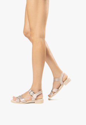 Sandales métalliques taupe avec design à brides croisées, boucle à la cheville et semelle plate beige. Texture lisse, polyvalentes pour un usage décontracté.