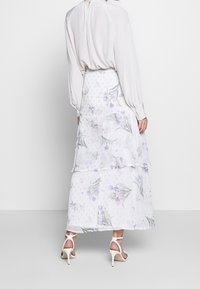 Weißer Maxirock mit Blumenmuster und Lagen-Design, mit violetten und grünen Mustern, halbtransparent, kombiniert mit weißen Riemchenabsätzen.