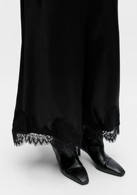 Black floor-length dress featuring a lace trim at the hem, paired with pointed black leather ankle boots. Smooth fabric texture.