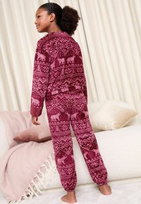 Conjunto de pijama burdeos con textura suave, decorado con patrones de animales blancos y geométricos, incluye una camiseta de manga larga y pantalones de tiro alto.
