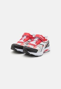 Zapatillas deportivas rojas y blancas con acentos negros, que cuentan con una correa de velcro, cordones y una marca visible en el costado y en la lengüeta.