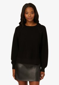 Maglione nero con dettagli intrecciati sulle spalle. Tessuto in maglia morbido e maniche lunghe, abbinato a una mini gonna in pelle nera lucida.