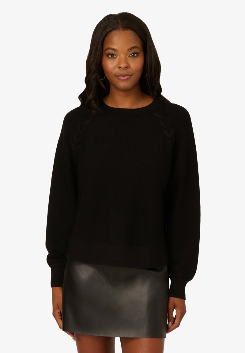 Maglione nero con dettagli intrecciati sulle spalle. Tessuto in maglia morbido e maniche lunghe, abbinato a una mini gonna in pelle nera lucida.