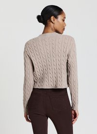 Pull en maille beige coupé, avec un col rond côtelé et des manches longues, associé à un jean foncé ajusté. Design minimaliste.
