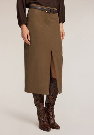 Olijfgroen suede midi-rok met een zijsplit, gecombineerd met bruin slangenprint kniehoogte laarzen en een donkere riem met een gouden gesp.