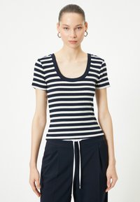 Marineblå og hvidstribet T-shirt med kort ærme, rund halsudskæring, ribbet tekstur og tætsiddende design. Sammen med mørke bukser med snoretræk.