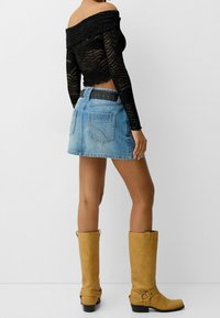 Černý top s dlouhým rukávem a odhalenými rameny spojený s světle modrou džínovou sukní. Oblečení je doplněno černým páskem s hroty a hnědými kozačkami po kolena.